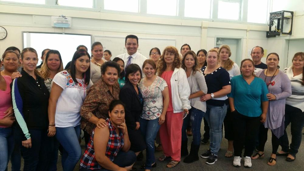 A group of adults students posing with their teacher in a classroom